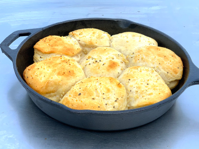 Eight cooked biscuits in a cast iron skillet sitting a gray-blueish table.